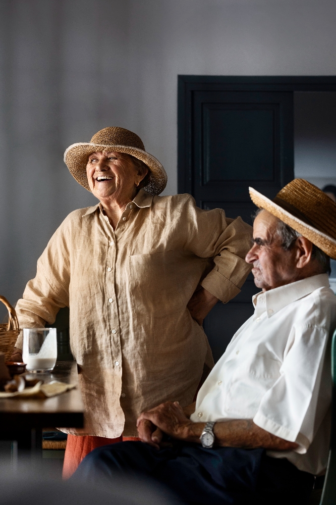 An elderly couple standing together outdoors in the countryside.